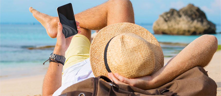 A man laying on the beach looking at bank alerts on his phone.