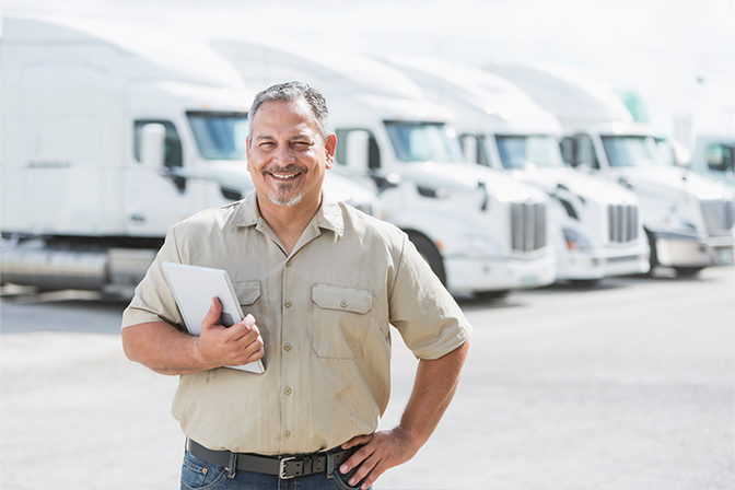 A fleet manager holding a tablet with a smile in front of trucks behind him