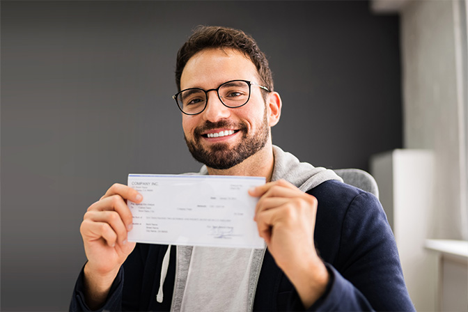 A smiling man holding a check toward the camera
