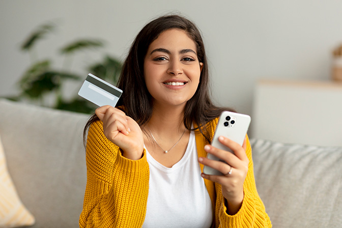 A woman in gold sweater holding a credit card and a phone