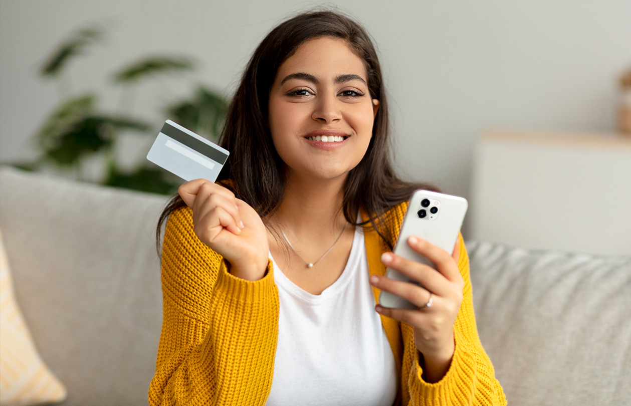 A woman in gold sweater holding a credit card and a phone