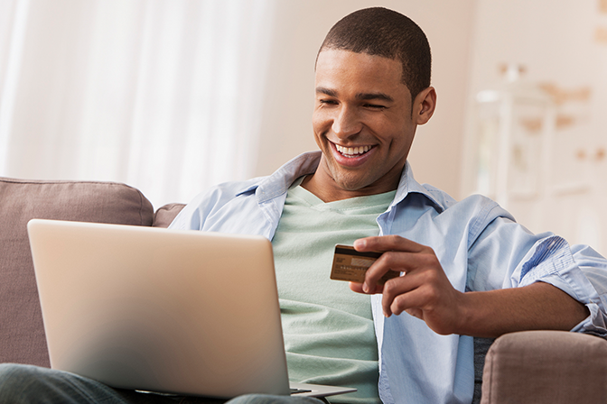 A man holding his credit card looking at a laptop with a smile