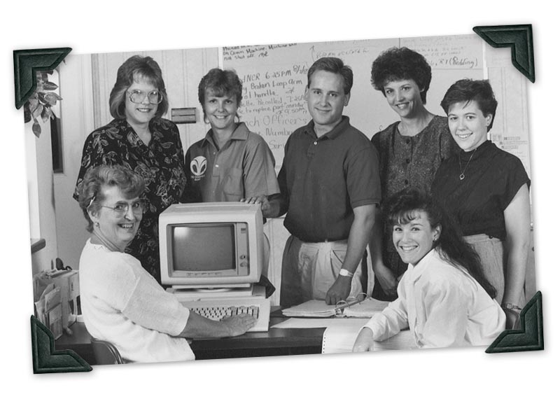 Seven tri counties bank employees smiling and standing around a desktop computer